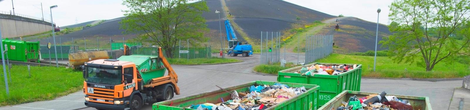 Ein Müllfahrzeug steht auf dem Betriebsgelände einer Deponie, im Vordergrund ein voller Container