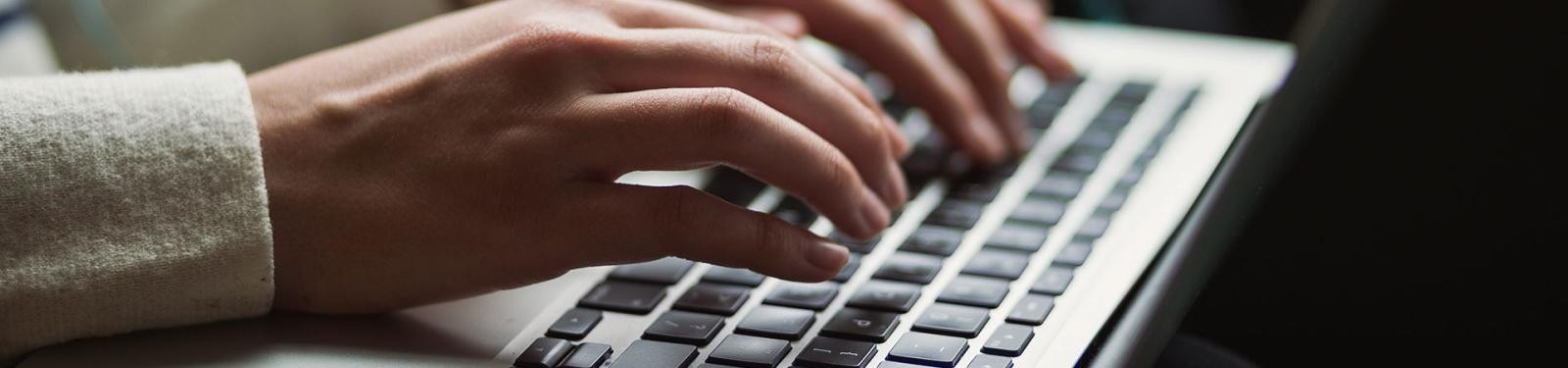 Formulare/Downloads Hände tippen etwas in einen geöffneten Laptop.