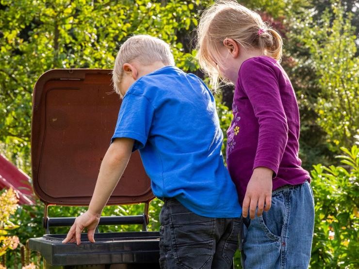 Biotonne im Sommer 2 kleine Kinder schauen in eine geöffnete Biotonne