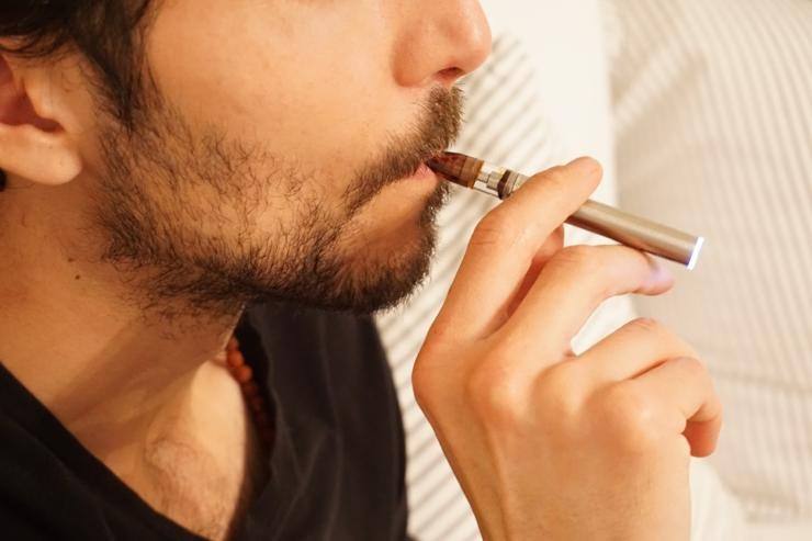 Ein Mann in einem schwarzen T-Shirt steht raucht eine Einmal-E-Zigarette 