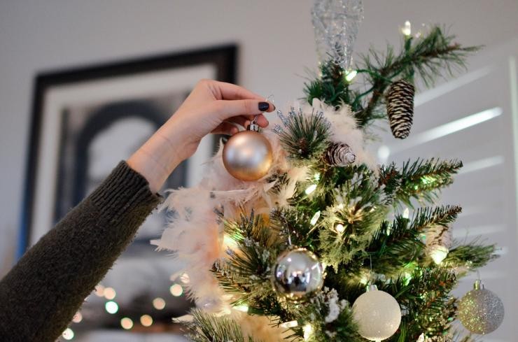 Eine Frau hängt eine Kugel an einen Weihnachtsbaumn Eine Frau hängt eine Kugel an einen Weihnachtsbaumn