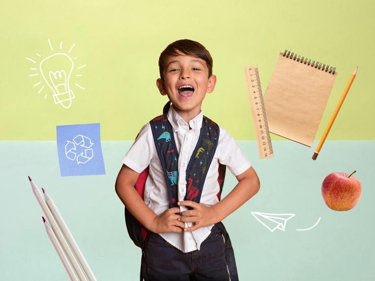 Junge lacht, um ihn herum verschiedene nachhaltige Schulmaterialien Junge lacht, um ihn herum verschiedene nachhaltige Schulmaterialien