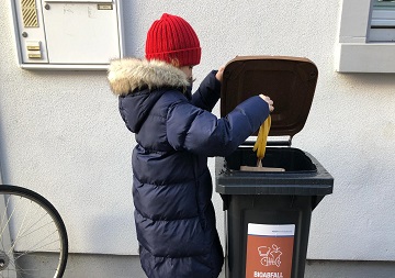 Ein Kind wirft eine Bananenschale in eine Biotonne