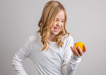 Kinderseite Ein Mädchen blickt auf ein Stück Obst in ihrer Hand und lacht.