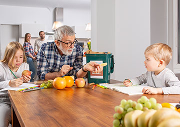 Ein älterer Mann sitzt mit zwei Kindern am Esstisch; auf dem Tisch befindet sich Obst und ein Bioabfallsammelbehälter