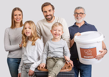 Eine Familie lächelt in die Kamera; der Großvater hält einen Bioabfallbehälter 