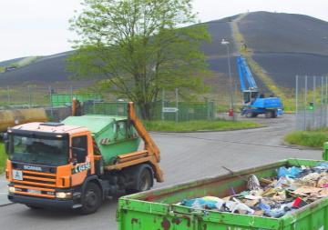 Ein Müllfahrzeug steht auf dem Betriebsgelände einer Deponie, im Vordergrund ein voller Container